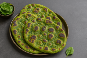 Wide-angle photo of freshly cooked spinach naan placed on a rustic wooden board, showing blistered, golden edges and vibrant green color—perfectly illustrating how to make spinach naan in a clay tandoor.