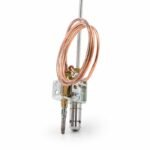 Gas Tandoor Pilot Assembly AS13 – close-up angled view of the pilot assembly bracket section on white background, showing the coiled copper thermocouple capillary tube, brass pilot gas jet, stainless steel pilot nozzle tube, igniter electrode with pointed tip, steel L-bracket mounting plate with bolt holes, and zinc-plated adjustment hardware, with the long stainless steel pilot tube rising out of frame at the top