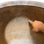 Tandoor Clay Pot Repair Kit AS08 – finger pointing to a network of cracks and fractures on the inner clay wall of a stainless steel-jacketed tandoor oven, highlighting the type of clay pot damage that the repair kit is designed to fix