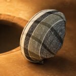 Tandoor Oven Naan Gaddi AS09 – dark green and black plaid woven naan gaddi resting upright on the warm terracotta rim of a tandoor oven, with the open oven mouth visible in the background bathed in golden heat, showing the gaddi in a resting position between uses