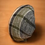 Tandoor Oven Naan Gaddi AS09 – side profile of a dome-shaped naan gaddi cushion upright on a warm wooden surface, showing dark green, black, and cream woven plaid fabric texture used to slap and press raw naan dough onto the tandoor clay wall