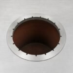 Tandoor Skewers Ring AS10 – overhead view of the stainless steel skewers ring installed around the opening of a dark clay-lined tandoor oven, showing all notch slots empty and the ring sitting flush against the brushed stainless steel oven top surface