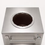 Tandoor Skewers Ring AS10 – elevated side view of the skewers ring installed on a Morni commercial stainless steel tandoor oven, showing the ring fitted into the oven opening with all slots empty, the NSF and ETL certification labels on the left panel, Morni branding and thermometer on the right panel, and the stainless steel pull handle on the front