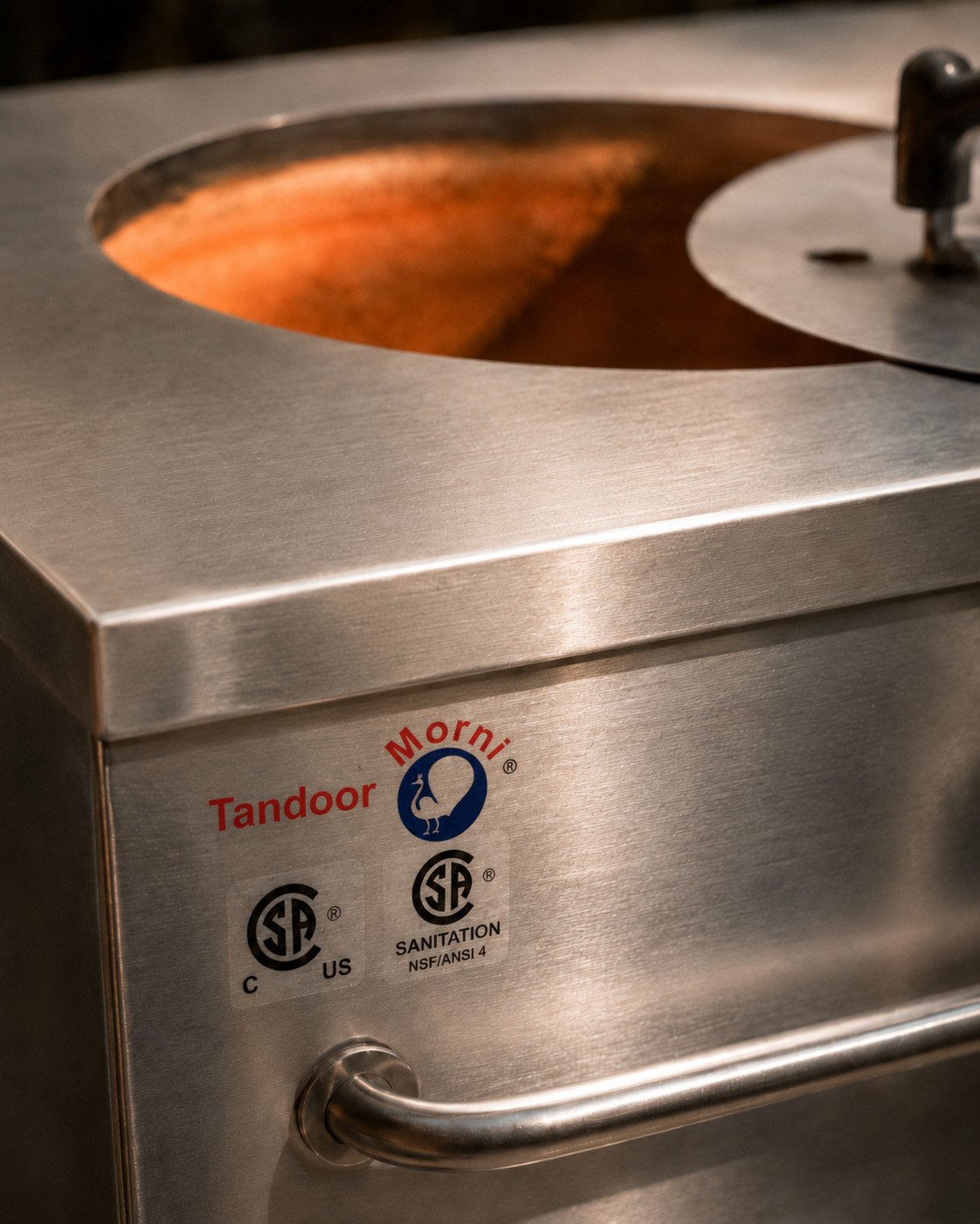 Close-up of a stainless steel tandoor oven for sale with Tandoor Morni branding, CSA certification, NSF/ANSI 4 sanitation label, and warm clay interior glow.